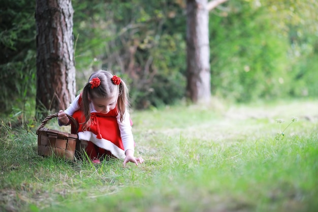 Foto ein kleines mädchen mit rotem hut und kleidern spaziert im park cosplay für den märchenhelden rotkäppchen