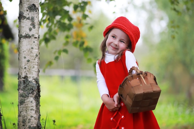 Ein kleines Mädchen mit rotem Hut und Kleidern spaziert im Park Cosplay für den Märchenhelden Rotkäppchen