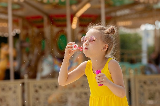 Ein kleines Mädchen mit Sonnenbrille bläst im Sommer Seifenblasen im Park