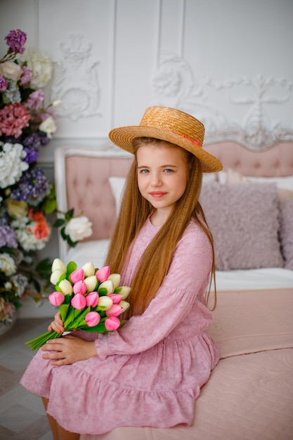 Ein kleines Mädchen mit Strohhut hält zu Hause einen Strauß Frühlingsblumen