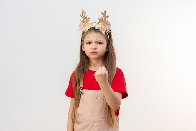 Ein kleines Mädchen mit Weihnachtshörnern zeigt ihre Faust und wird wütend.