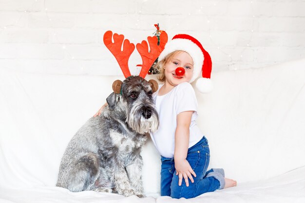 Ein kleines Mädchen mit Weihnachtsmannmütze sitzt mit ihrem geliebten Hund auf der Couch