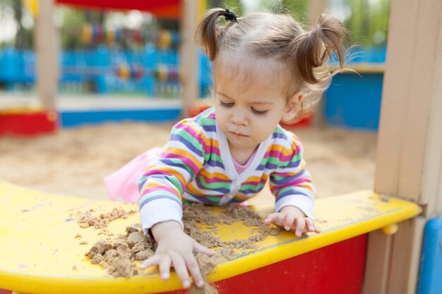 Ein kleines Mädchen mit zwei Schwänzen, die im Sandkasten auf dem Spielplatz spielen