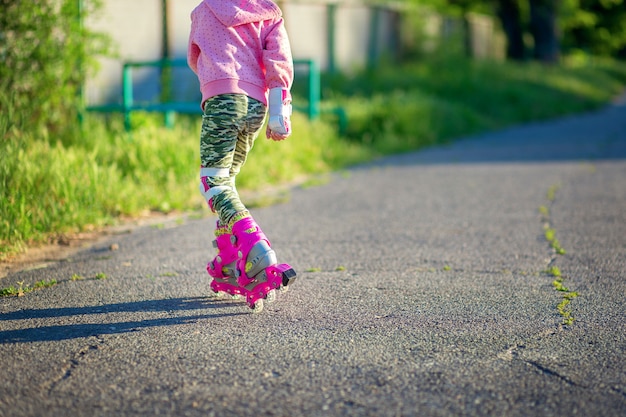 Ein kleines Mädchen reitet auf rosa Rollschuhen auf Asphalt