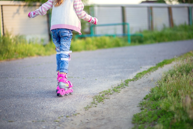 Ein kleines Mädchen reitet auf rosa Rollschuhen auf Asphalt