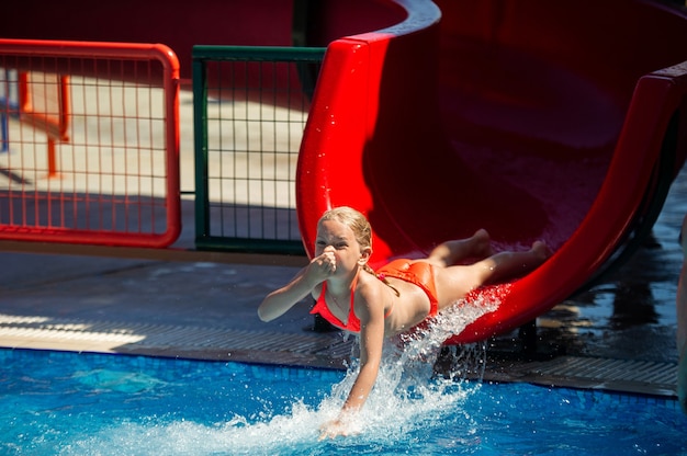 Ein kleines Mädchen rutscht während der Sommerferien eine Wasserrutsche hinunter in einen Pool in einem Wasserpark.