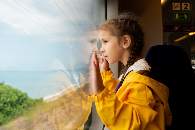 Ein kleines Mädchen schaut aus dem Fenster eines Zuges auf das Meer Reise Reflexion Sommer Familienurlaub