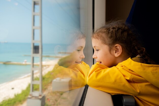 Ein kleines Mädchen schaut aus dem Fenster eines Zuges auf das Meer Reise Reflexion Sommer Familienurlaub