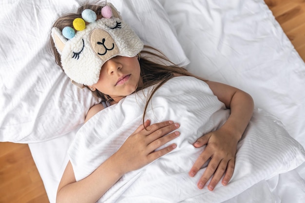 Ein kleines Mädchen schläft auf einem Kissen mit einer lustigen Schlafmaske