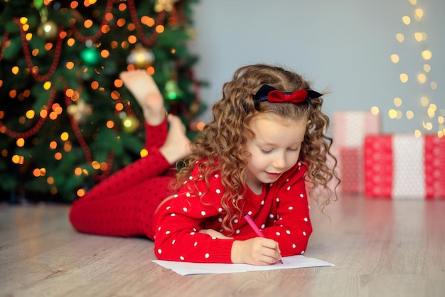 ein kleines Mädchen schreibt einen Brief an den Weihnachtsmann nach Hause in der Nähe des Weihnachtsbaums