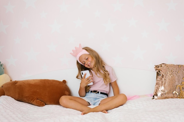 Ein kleines Mädchen sitzt auf dem Bett, hält ein Telefon in den Händen und spricht auf einem Smartphone