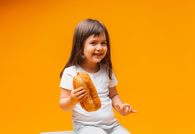Ein kleines Mädchen sitzt auf einem Würfel auf gelbem Hintergrund und isst ein gesundes Brot aus Naturprodukten