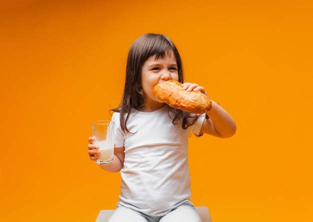 Ein kleines Mädchen sitzt auf einem Würfel auf gelbem Hintergrund und isst ein gesundes Brot aus Naturprodukten