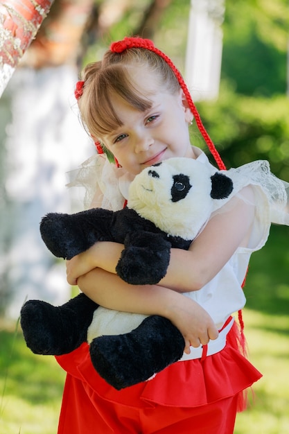 Ein kleines Mädchen sitzt im Sommer mit einem Spielzeugpanda in der Natur. Foto in hoher Qualität