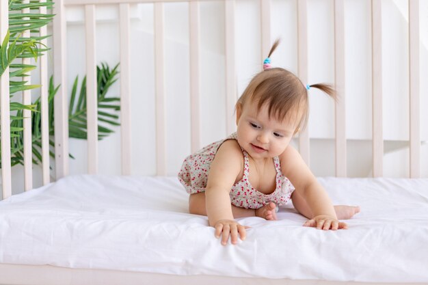 Ein kleines Mädchen sitzt in einem hellen Raum in einem Kinderbett