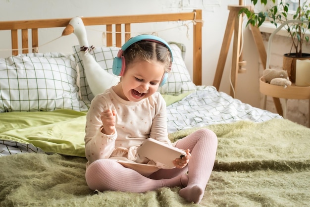 Ein kleines Mädchen sitzt mit Kopfhörern auf dem Bett und spielt rücksichtslos Spiele und hört Musik