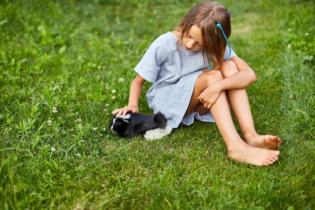 Ein kleines Mädchen spielt mit dem schwarzen Meerschweinchen, das im Sommer draußen sitzt