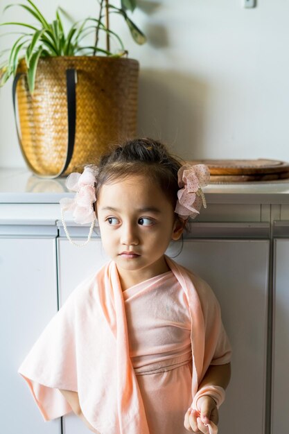 Foto ein kleines mädchen steht in einem wunderschönen kleid mit haaraccessoires und tut so, als würde es zu hause spielen.