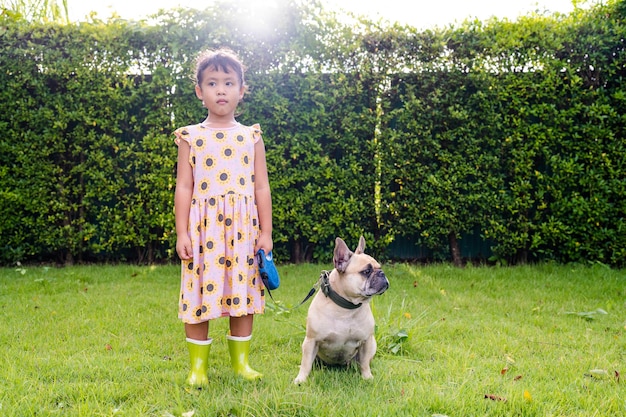 Ein kleines Mädchen steht mit einem Hund an der Leine in einem Garten.