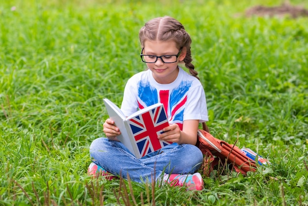 Ein kleines Mädchen studiert ein Englischbuch, während es auf dem Rasen sitzt.