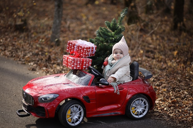 Ein kleines Mädchen trägt einen Weihnachtsbaum und Geschenke in einem roten Auto