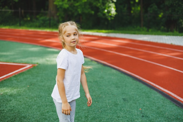 Ein kleines Mädchen treibt Sport auf dem Rasen, das Kind wärmt sich vor dem Training im Stadion auf Kindersport und gesunder Lebensstil