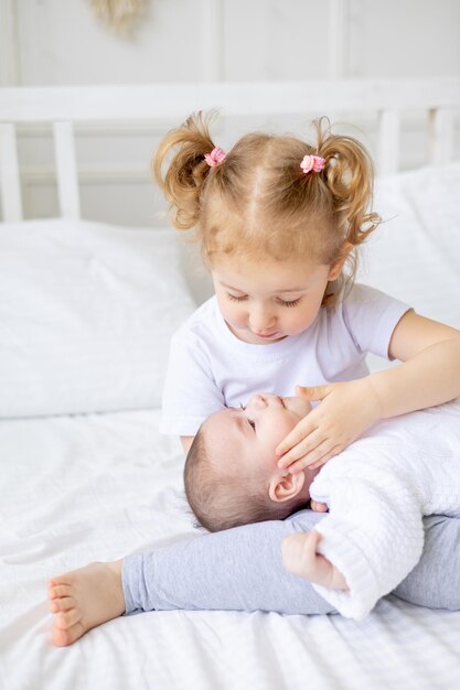 Ein kleines Mädchen umarmt eine neugeborene Schwester oder einen neugeborenen Bruder auf einem weißen Bett zu Hause zwei Kinder in der Familie