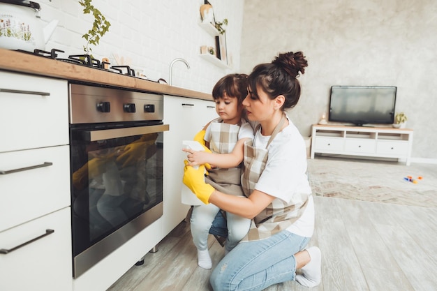 Ein kleines Mädchen und ihre Mutter putzen die Küche, eine Frau und ein Kind wischen den Ofen in der Küche ab und helfen der Mutter beim Putzen