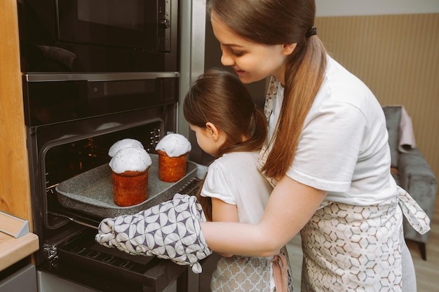 Ein kleines Mädchen und ihre Mutter stellen ein Formular mit Osterkuchen in den Ofen in der Küche. Mutter und Kind kochen gemeinsam Osterkuchen in der Küche