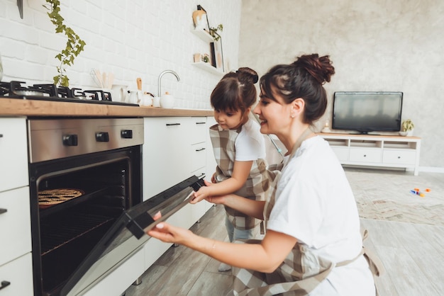 Ein kleines Mädchen und ihre Mutter stellen eine Auflaufform mit einem Kuchen in den Ofen in der Küche. Mutter und Kind kochen zusammen einen Kuchen in der Küche