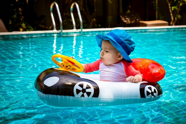 Ein kleines Mädchen unter einem Jahr fährt ein Schlauchboot in Form eines Autos im Pool