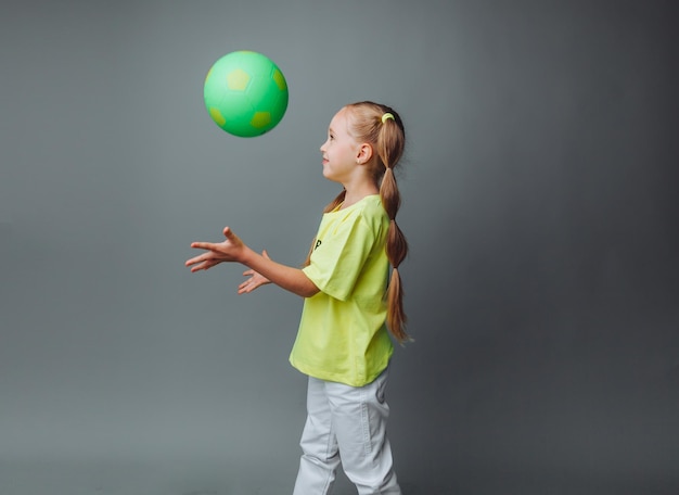 Ein kleines Mädchen wirft einen Ball isoliert auf grauem Hintergrund ein kleiner AthletKindersport