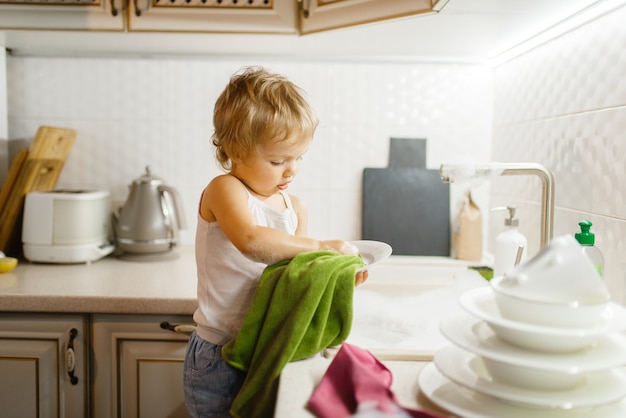 Ein kleines Mädchen wischt das Geschirr in der Küche ab. Baby macht Hausarbeit zu Hause.