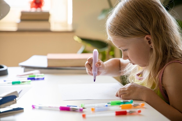 Ein kleines Mädchen zieht mit einem Marker, während es am Tisch sitzt