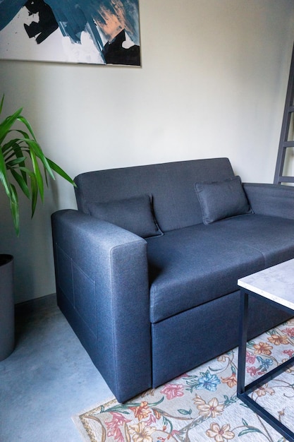 Ein kleines modernes Sofa in Blau und Grau neben einer Palme in einer Wanne und einem kleinen Tisch im Loftstil