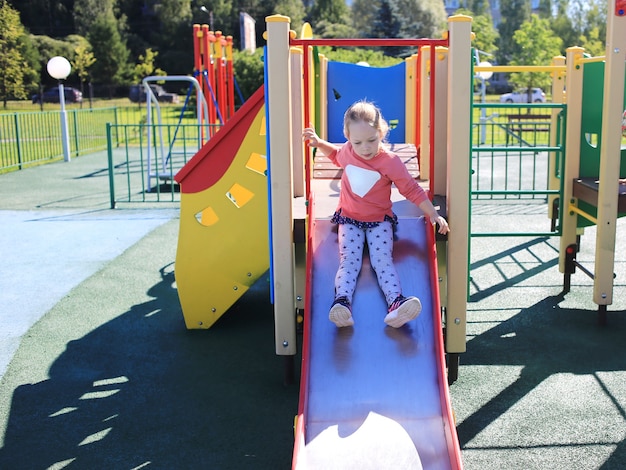 Ein kleines schönes Mädchen rollt auf einem Hügel auf einem Kinderspielplatz.