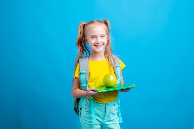 Ein kleines Schulmädchen hält ein Buch und einen Apfel auf blauem Hintergrund