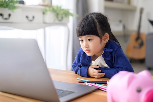 Ein kleines süßes Mädchen benutzt einen Laptop, um zu Hause online über das Internet zu lernen. E-Learning-Konzept während der Quarantänezeit.