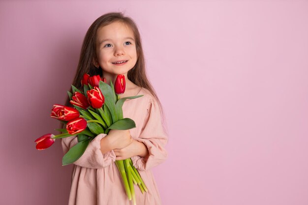 Ein kleines süßes Mädchen, das einen Strauß Tulpen hält Rosa Hintergrund Happy Womens Day Platz für Text