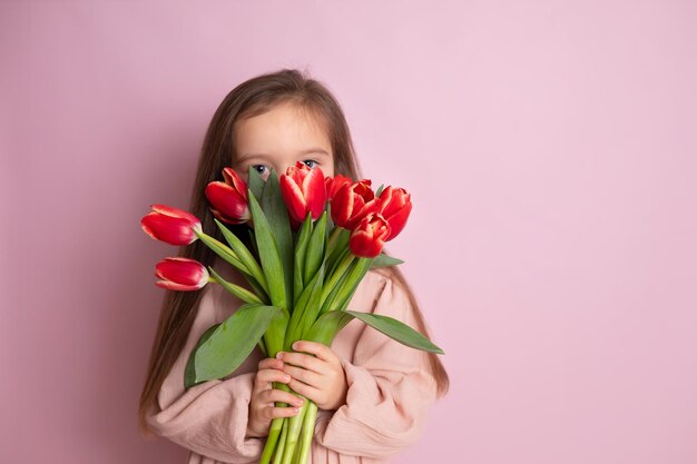 Ein kleines süßes Mädchen, das einen Strauß Tulpen hält und sie schnüffelt Rosa Hintergrund. Alles Gute zum Tag der Frauen. Platz für Text. Helle Emotionen. Foto in hoher Qualität