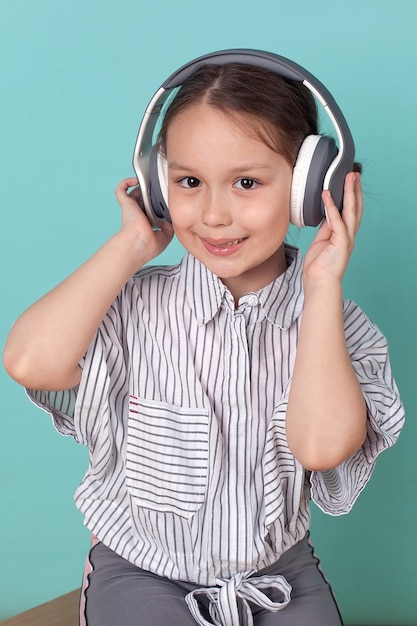 Ein kleines süßes Mädchen hört Musik mit großen Kopfhörern auf blauem Hintergrund.