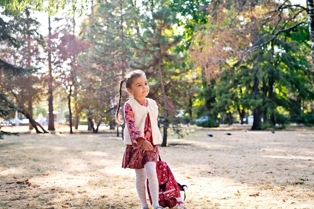 ein kleines süßes mädchen in einem roten kleid ein schulmädchen spaziert mit einem rucksack in einem herbstpark