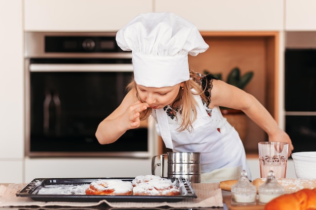 Foto ein kleines süßes mädchen mit weißer kochmütze schmeckt gebäck in der küche