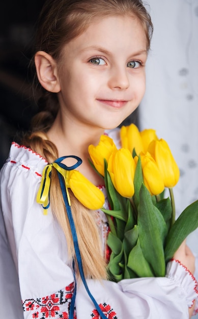 Ein kleines ukrainisches Mädchen in traditioneller Kleidung hält gelbe Tulpen in ihren Händen
