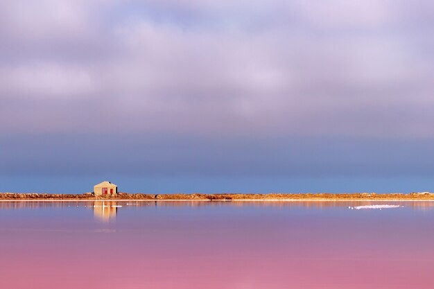 Ein kleines verlassenes Steinhaus steht auf einem rosa Salzsee unter strahlend blauem Himmel