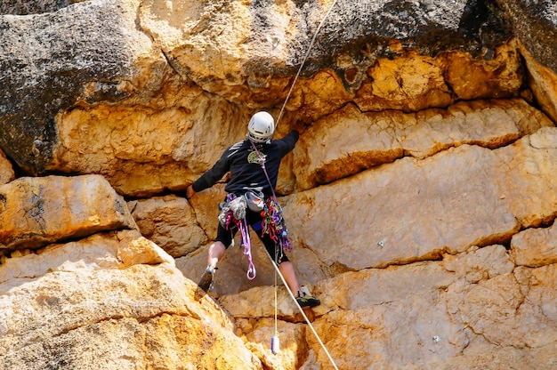 Ein Kletterer mit einem Sicherheitsseil, der auf einem flachen Felsen mit Rissen und Rillen in der Oberfläche klettert