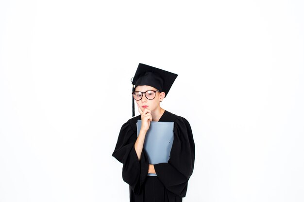 Ein kluger Student mit akademischem Hut und Brille steht mit Büchern