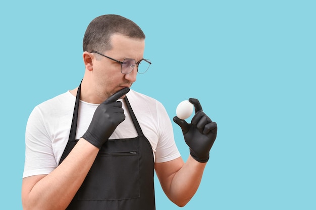 Ein Koch in einer Schürze hält ein frisches Ei auf blauem Hintergrund und denkt über eine Frage zum Kochen nach
