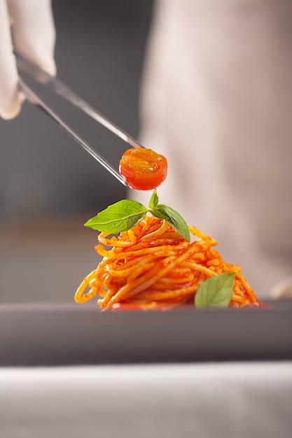 Ein Koch in weißer Uniform und Handschuhen serviert Kirschtomaten in Pasta in Tomatensauce mit Pinzette