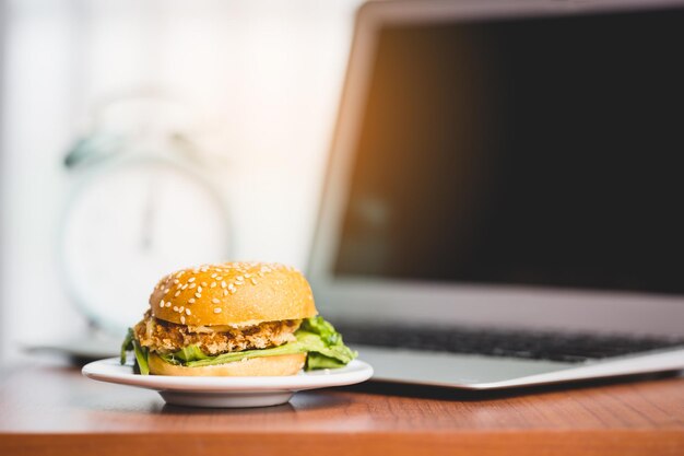 Foto ein köstlicher hamburger auf dem tisch mit einem verschwommenen laptop und einem wecker